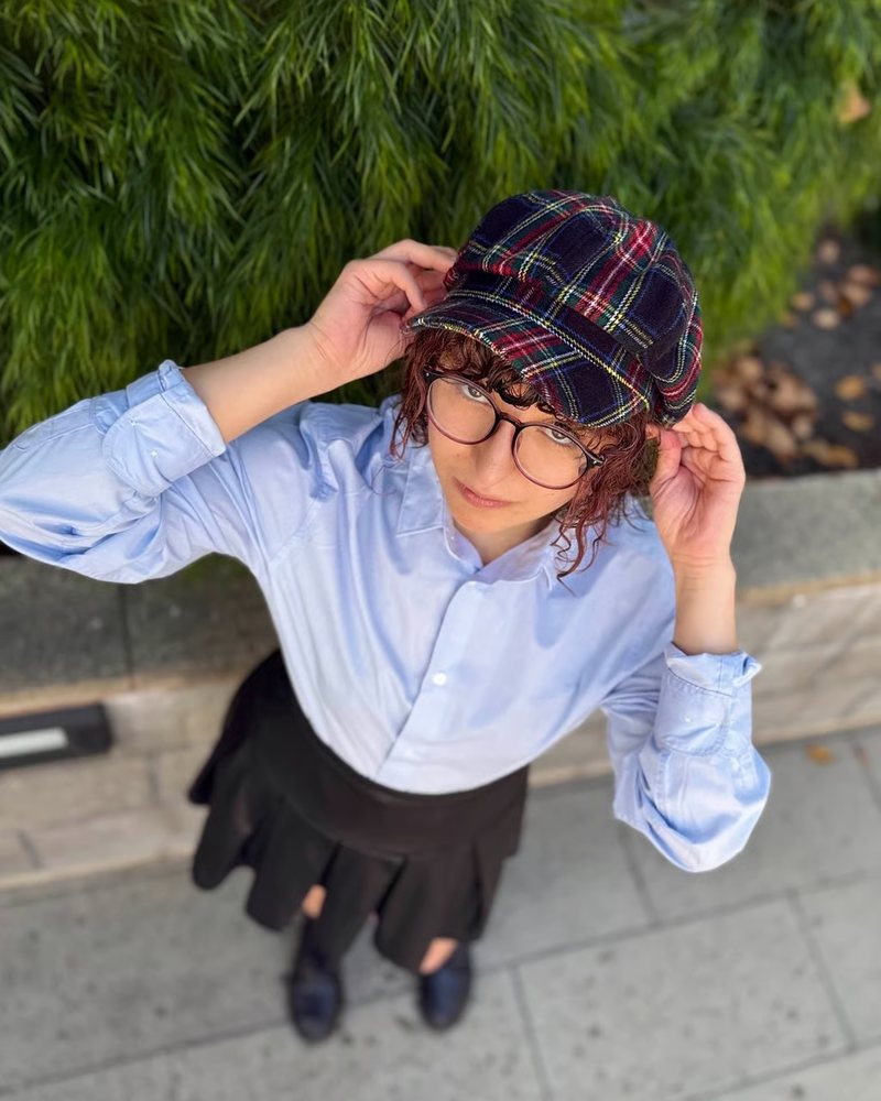 Trishia Nunez in a plaid newsboy cap, round glasses and a light blue shirt, photographed from above